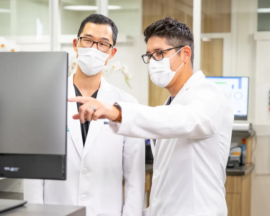 Two Fresno Oral Surgery surgeons in white coats and masks at a workstation, one pointing to the screen as they review a case together