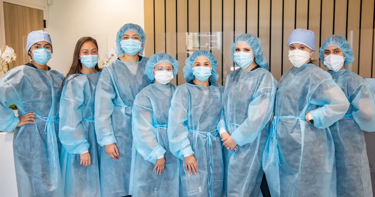 Ten members of the Fresno Oral Surgery clinical staff standing together in blue gowns, caps and masks in the office